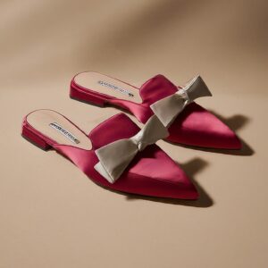 A close up shot of a pair of pink women's mules with a white ribbon design.